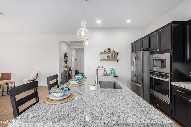 kitchen with light stone counters, stainless steel appliances, a kitchen island with sink, and sink