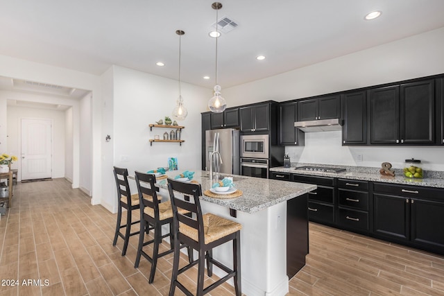 kitchen with hanging light fixtures, appliances with stainless steel finishes, a breakfast bar, and a center island with sink