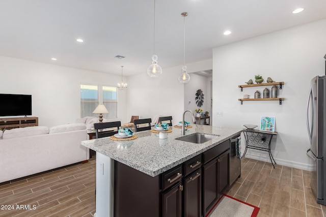 kitchen with sink, decorative light fixtures, an island with sink, stainless steel appliances, and light stone countertops