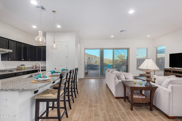 kitchen featuring decorative light fixtures, sink, a breakfast bar area, stainless steel gas cooktop, and light wood-type flooring