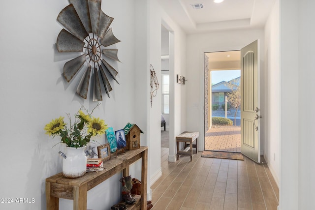 doorway to outside featuring a tray ceiling and light hardwood / wood-style floors