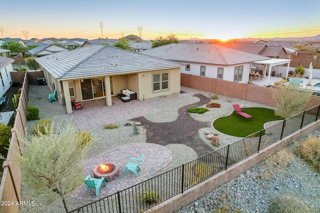 back house at dusk with a fire pit, a patio area, and a lawn