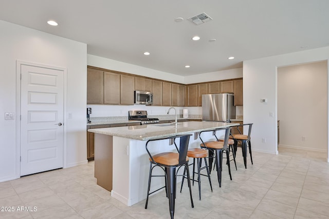 17819 W Georgia Ave, Litchfield Park, AZ 85340 - kitchen featuring stainless steel appliances, an island with sink, recessed lighting, a kitchen bar, and light stone countertops