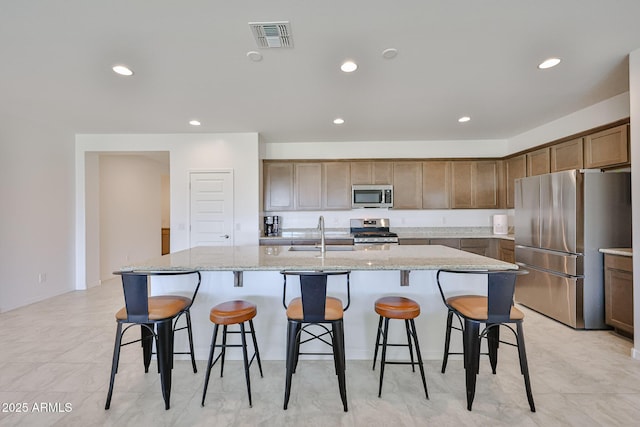 17819 W Georgia Ave, Litchfield Park, AZ 85340 - kitchen featuring appliances with stainless steel finishes, a center island with sink, light stone counters, recessed lighting, and a breakfast bar area