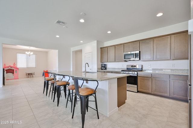 17819 W Georgia Ave, Litchfield Park, AZ 85340 - kitchen featuring stainless steel appliances, a chandelier, a kitchen island with sink, a breakfast bar, and light stone counters