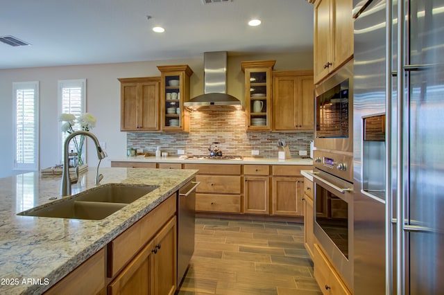 kitchen featuring appliances with stainless steel finishes, backsplash, sink, wall chimney range hood, and hardwood / wood-style floors