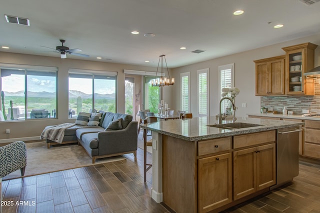 kitchen with light stone countertops, sink, a mountain view, an island with sink, and ceiling fan with notable chandelier