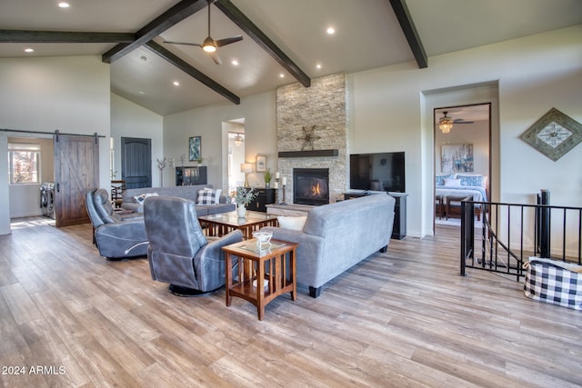 living room with a fireplace, a barn door, high vaulted ceiling, and light wood-type flooring