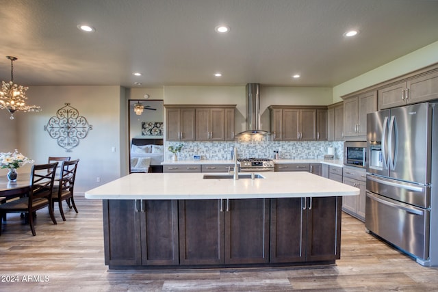 kitchen with wall chimney exhaust hood, sink, appliances with stainless steel finishes, and light wood-type flooring