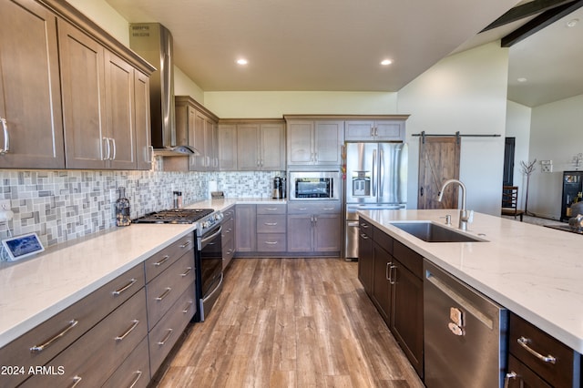 kitchen with hardwood / wood-style floors, a barn door, sink, wall chimney exhaust hood, and stainless steel appliances