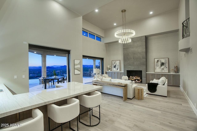 living room featuring a chandelier, light wood-type flooring, a mountain view, a towering ceiling, and a fireplace