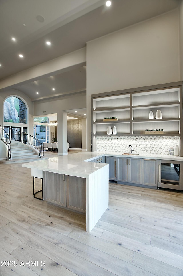 kitchen with sink, kitchen peninsula, beverage cooler, light hardwood / wood-style floors, and backsplash