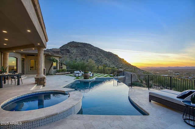 pool at dusk featuring an in ground hot tub, a mountain view, and a patio