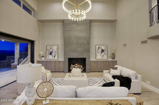 living room with a tiled fireplace, a high ceiling, an inviting chandelier, and light wood-type flooring