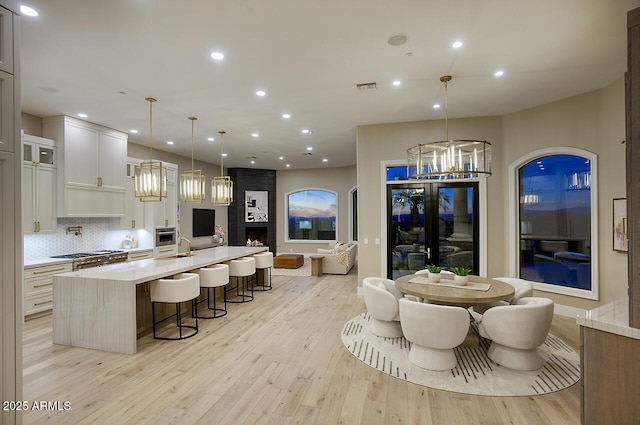 kitchen with a large island, white cabinetry, a kitchen breakfast bar, decorative backsplash, and decorative light fixtures