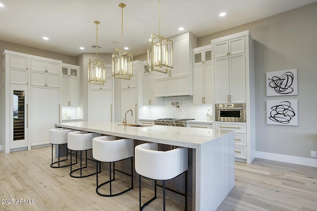 kitchen with pendant lighting, sink, a kitchen island with sink, backsplash, and white cabinets