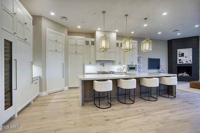 kitchen featuring a breakfast bar, pendant lighting, decorative backsplash, light wood-type flooring, and a spacious island