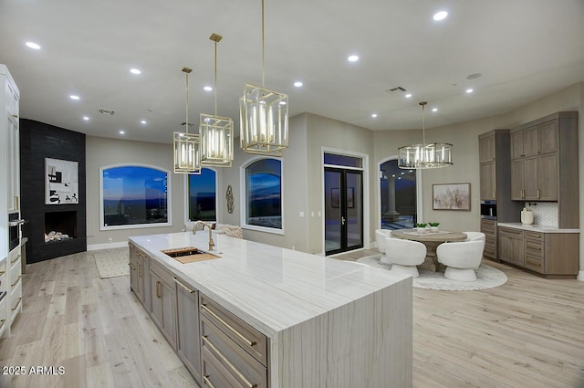 kitchen featuring pendant lighting, sink, light hardwood / wood-style flooring, a large fireplace, and a large island with sink