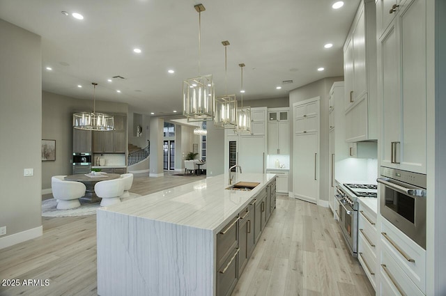 kitchen featuring a large island with sink, white cabinetry, sink, and pendant lighting