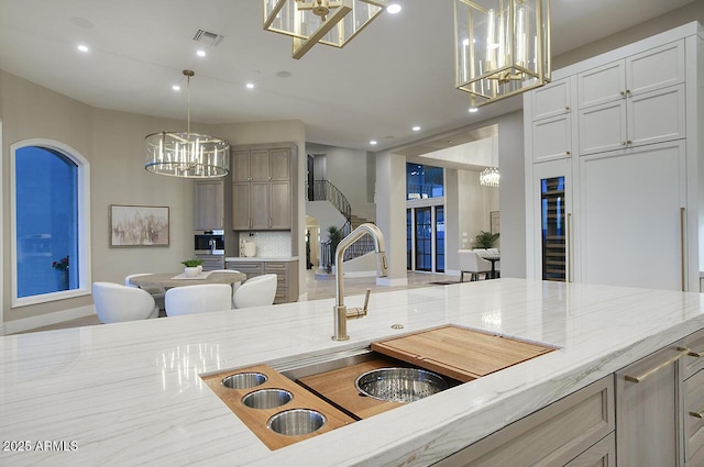 kitchen featuring pendant lighting, sink, light stone counters, a chandelier, and light brown cabinets