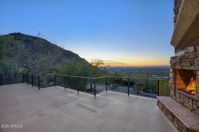 patio terrace at dusk featuring a mountain view and an outdoor stone fireplace