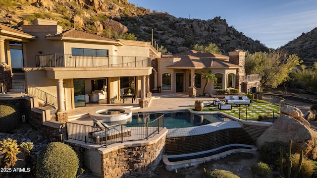 back of property featuring a patio, an outdoor living space, a pool with hot tub, a mountain view, and a balcony