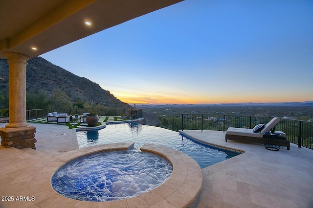 pool at dusk featuring a mountain view, a patio area, and an in ground hot tub