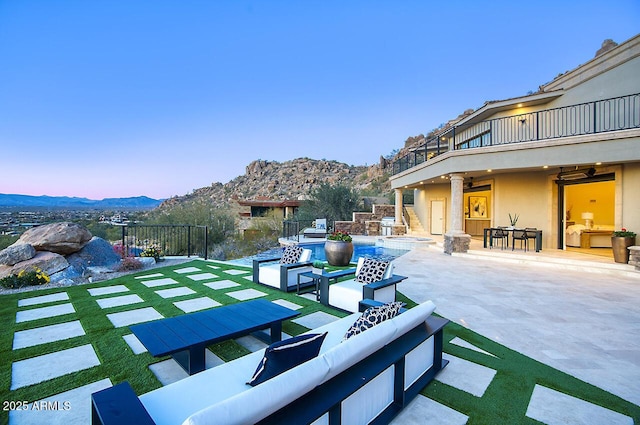 patio terrace at dusk featuring a mountain view, outdoor lounge area, a balcony, and ceiling fan