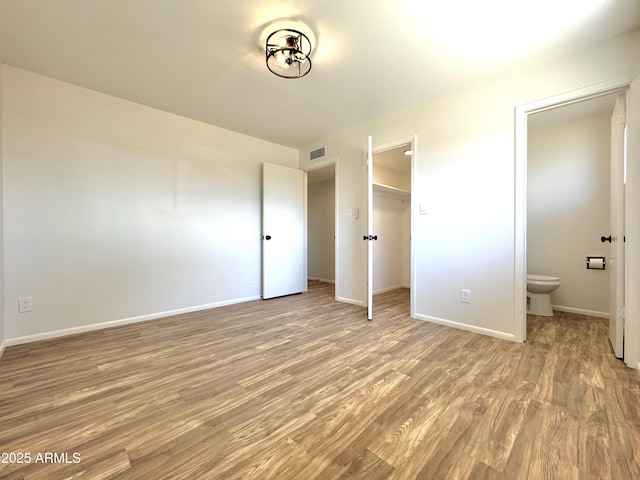 unfurnished bedroom featuring visible vents, a closet, connected bathroom, light wood-style floors, and baseboards