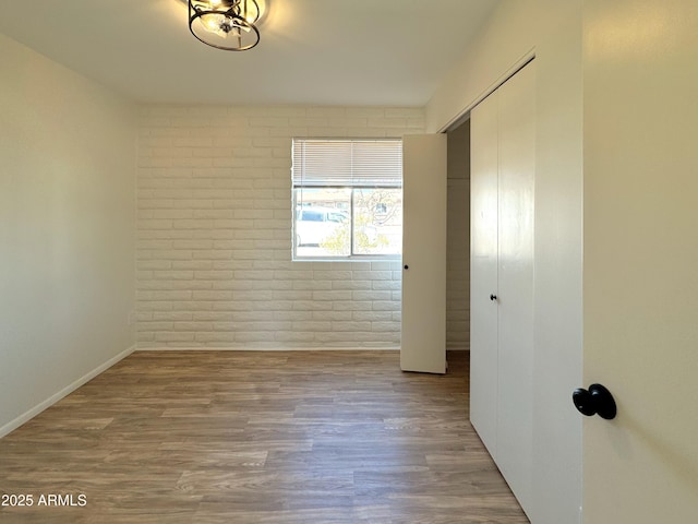 spare room with brick wall and wood finished floors