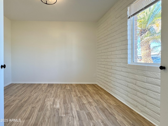 spare room featuring brick wall, baseboards, and wood finished floors