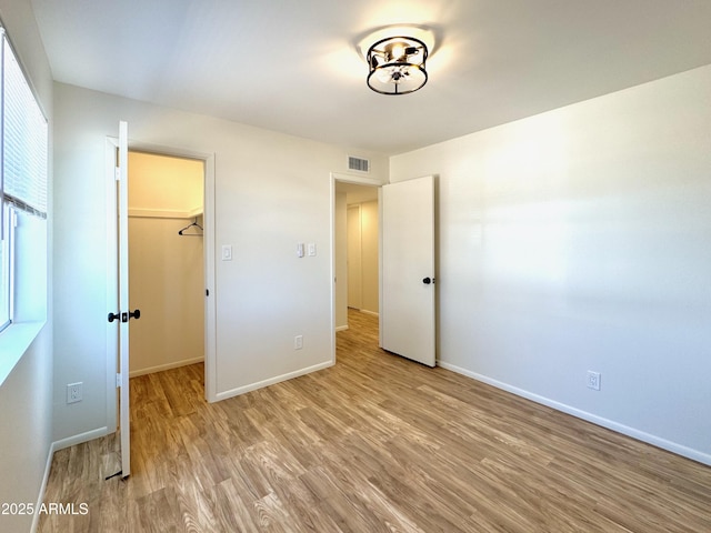 unfurnished bedroom with baseboards, visible vents, a closet, a walk in closet, and light wood-type flooring