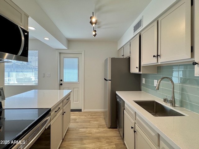 kitchen featuring visible vents, a sink, decorative backsplash, stainless steel appliances, and light wood-style floors