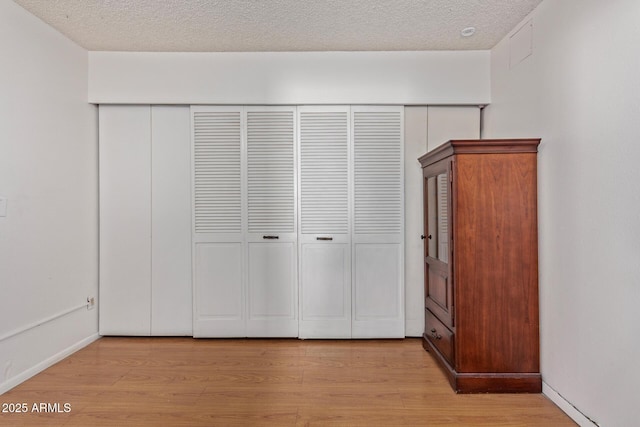 unfurnished bedroom with a closet, a textured ceiling, and light wood-type flooring