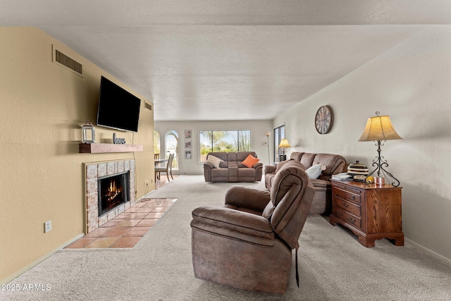 living area with visible vents, carpet flooring, a textured ceiling, a tile fireplace, and baseboards