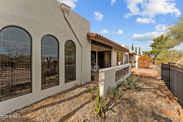 view of side of property with a tile roof, fence, and stucco siding