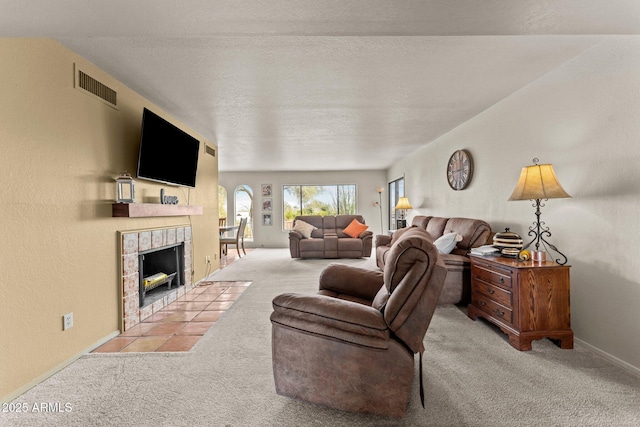 living room featuring a textured ceiling, carpet floors, a tiled fireplace, and visible vents