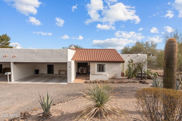 view of front facade with dirt driveway, a tiled roof, a chimney, and stucco siding