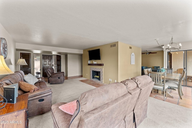 carpeted living area with ceiling fan with notable chandelier, visible vents, a textured ceiling, and a tile fireplace