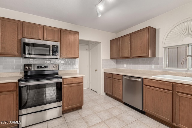 kitchen featuring stainless steel appliances, a sink, light countertops, and brown cabinets