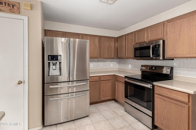 kitchen with light tile patterned floors, appliances with stainless steel finishes, brown cabinets, light countertops, and backsplash