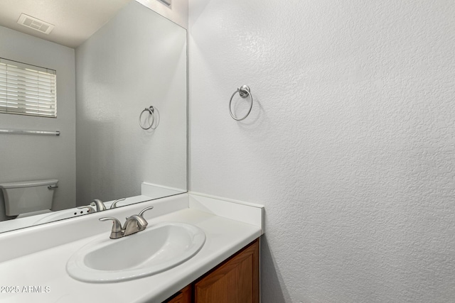 bathroom featuring toilet, vanity, visible vents, and a textured wall