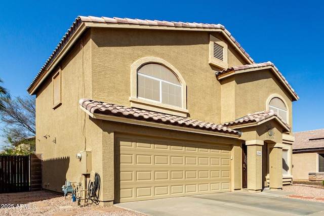 mediterranean / spanish home featuring a tile roof, stucco siding, concrete driveway, an attached garage, and fence