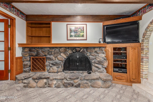 unfurnished living room with a stone fireplace, a textured ceiling, carpet floors, built in features, and beam ceiling