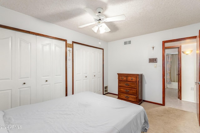 carpeted bedroom featuring ceiling fan, two closets, and a textured ceiling