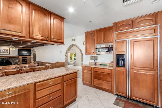 kitchen with ceiling fan, light stone counters, paneled refrigerator, a fireplace, and light tile patterned flooring