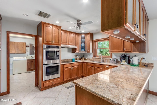 kitchen featuring sink, light stone counters, kitchen peninsula, stainless steel double oven, and washer / clothes dryer