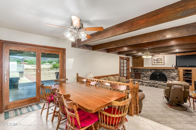 dining space with light tile patterned flooring, ceiling fan, beam ceiling, and a fireplace