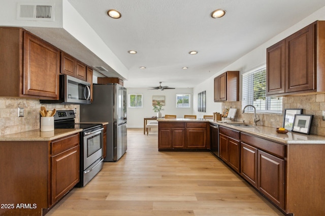 kitchen featuring visible vents, a peninsula, a sink, light wood-style flooring, and stainless steel appliances