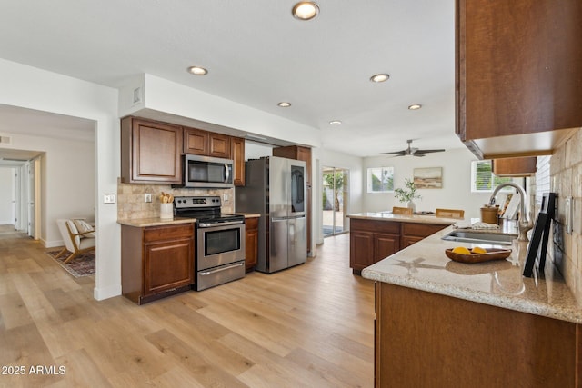 kitchen with backsplash, stainless steel appliances, a sink, and light wood-style flooring